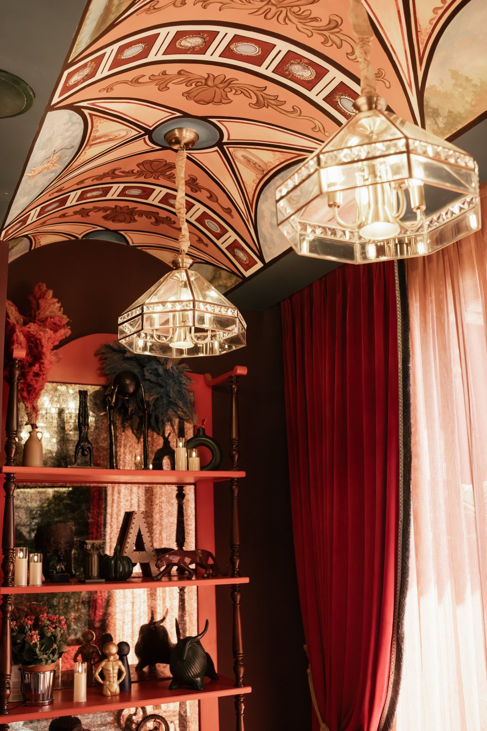 A studio corner with a red curtain, shelves of curios and a pair of crystal lamps