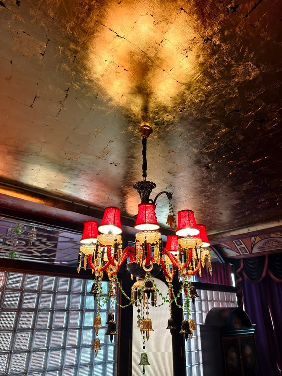 A chandelier with red shades against a gilded ceiling